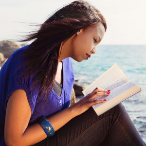 Woman reading bible at seashore.